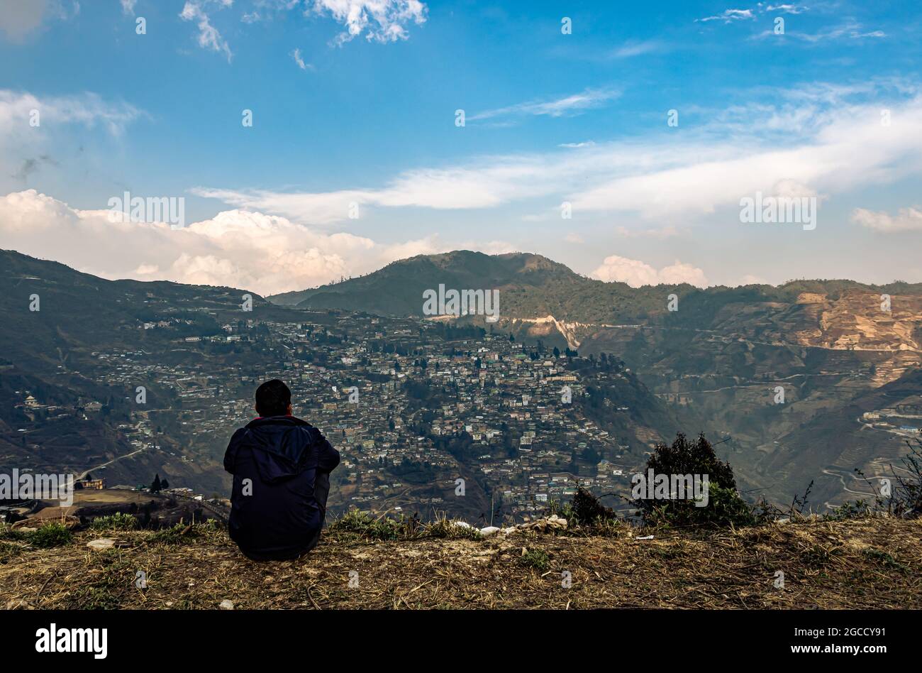 Mann, der am oberen Rand des Berges mit überfüllter Stadtstruktur und erstaunlicher Himmel am Abend sitzt, wird am Bombenangriff arunachal pradesh india aufgenommen. Stockfoto