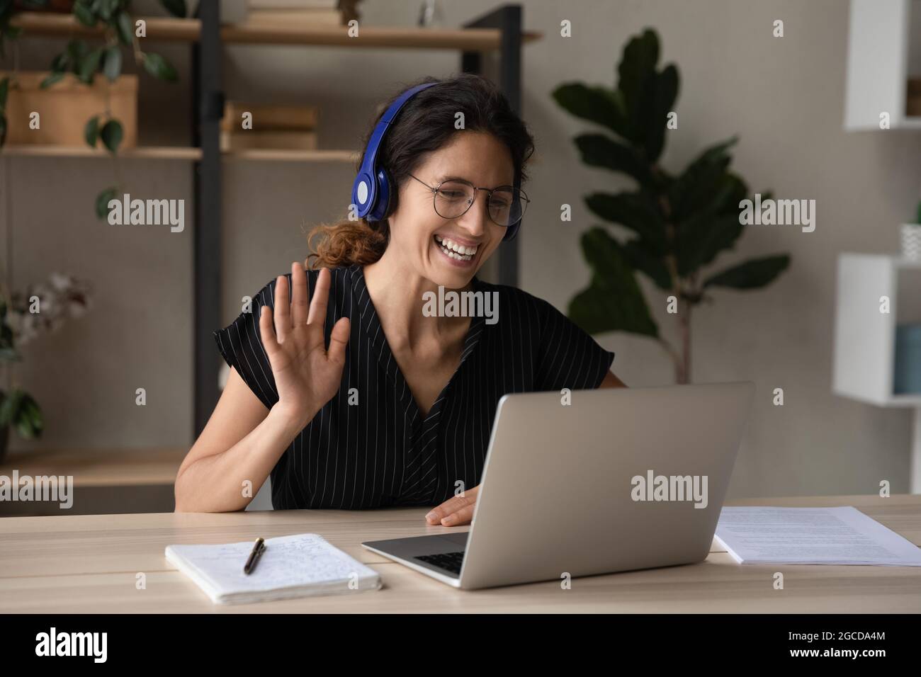 Nahaufnahme lächelnde Frau in Kopfhörern, die Hand an die Webcam schwenkt Stockfoto