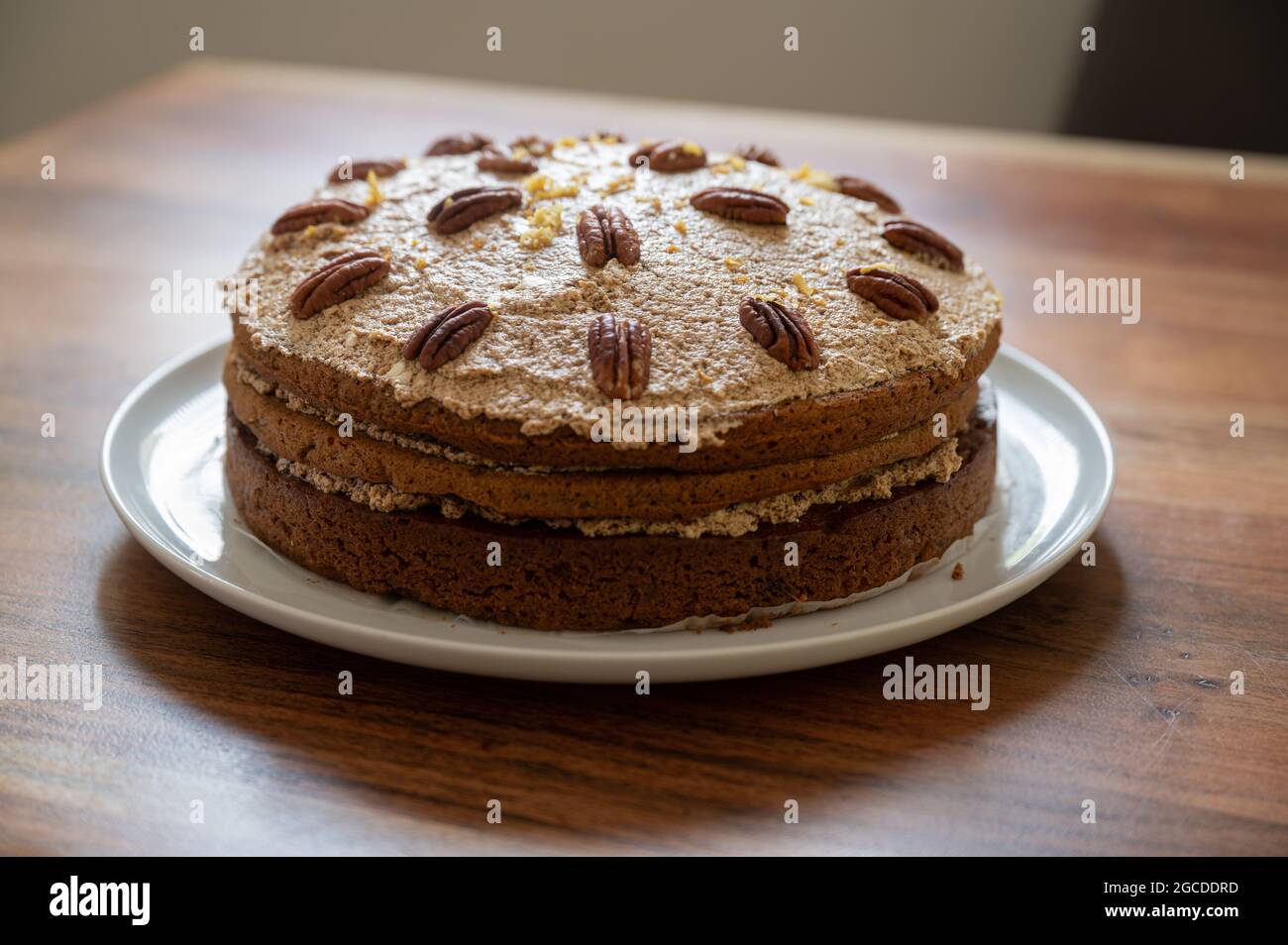 Schöner veganer Karottenkuchen mit Glasur und verzierten Pekannüssen auf einem Holztisch. Stockfoto