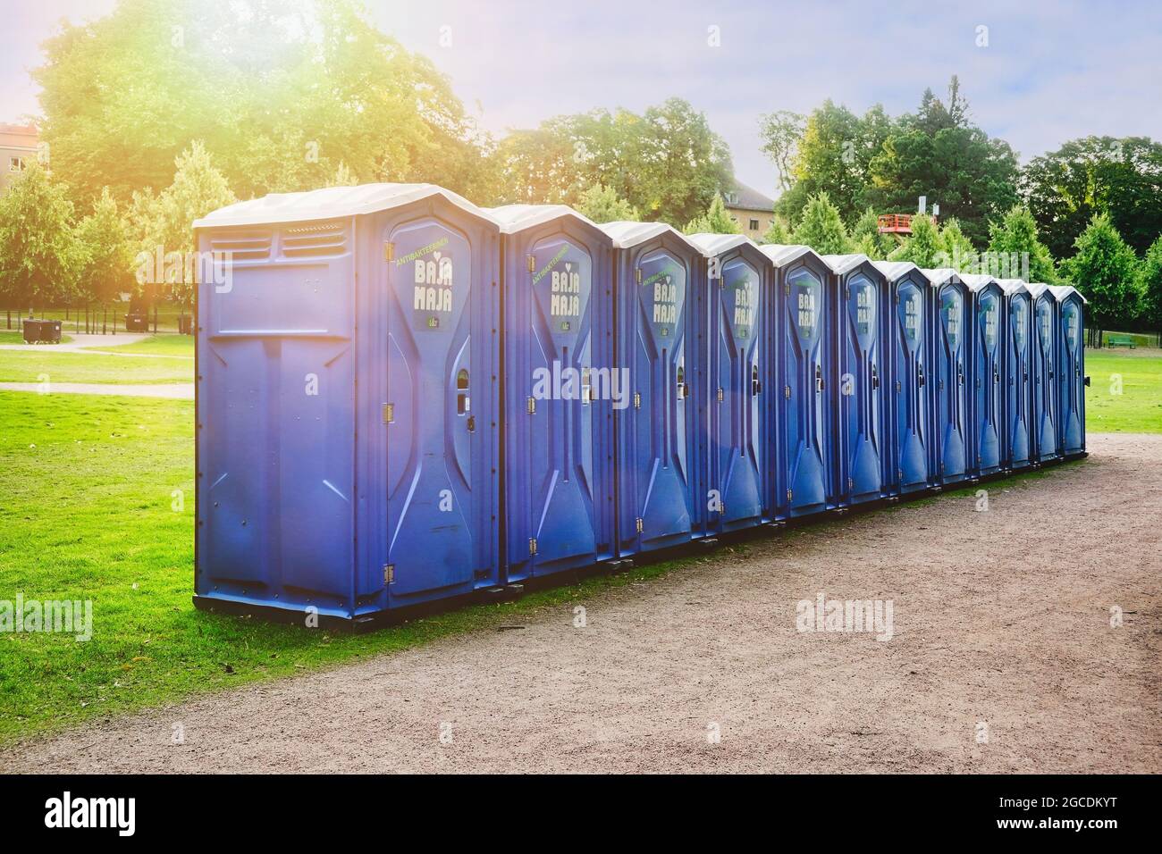 Reihe von zwölf blauen Bajamaja-tragbaren Toiletten im Park für einen Veranstaltungsort im Freien. Helsinki, Finnland. 7. August 2021. Stockfoto