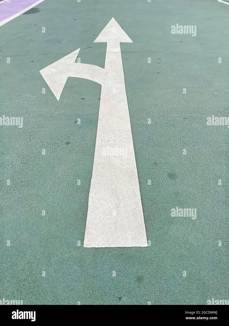 Einfach ein Abbiegekonzept treffen: Weißer isolierter Pfeil auf grünem Bürgersteig, der die Richtung geradeaus oder links zeigt Stockfoto