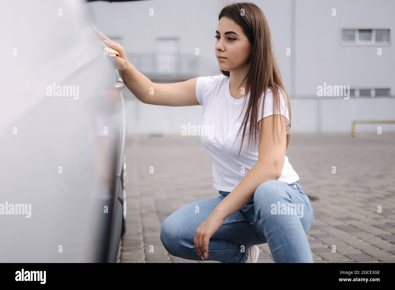 Vorderansicht der attraktiven fröhlichen weiblichen Fahrerin, die ihr Auto mit einem speziellen Lappen in der Selbstbedienungswaschung gewaschen hat Stockfoto