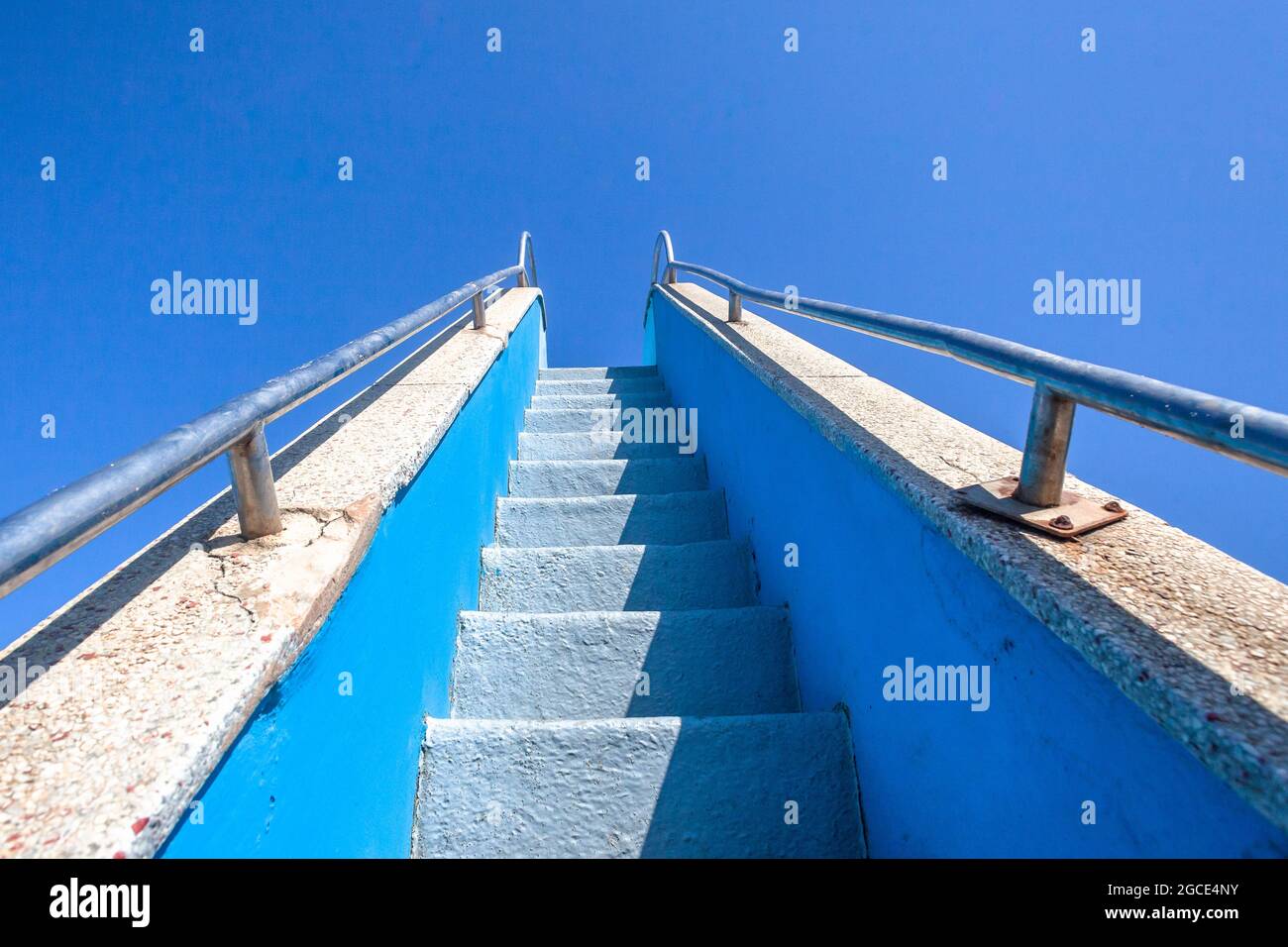 Schmale Stufen nach oben mit Edelstahlgeländern nach oben zum blauen Himmel an der Wasserrutsche des öffentlichen Schwimmbads. Stockfoto