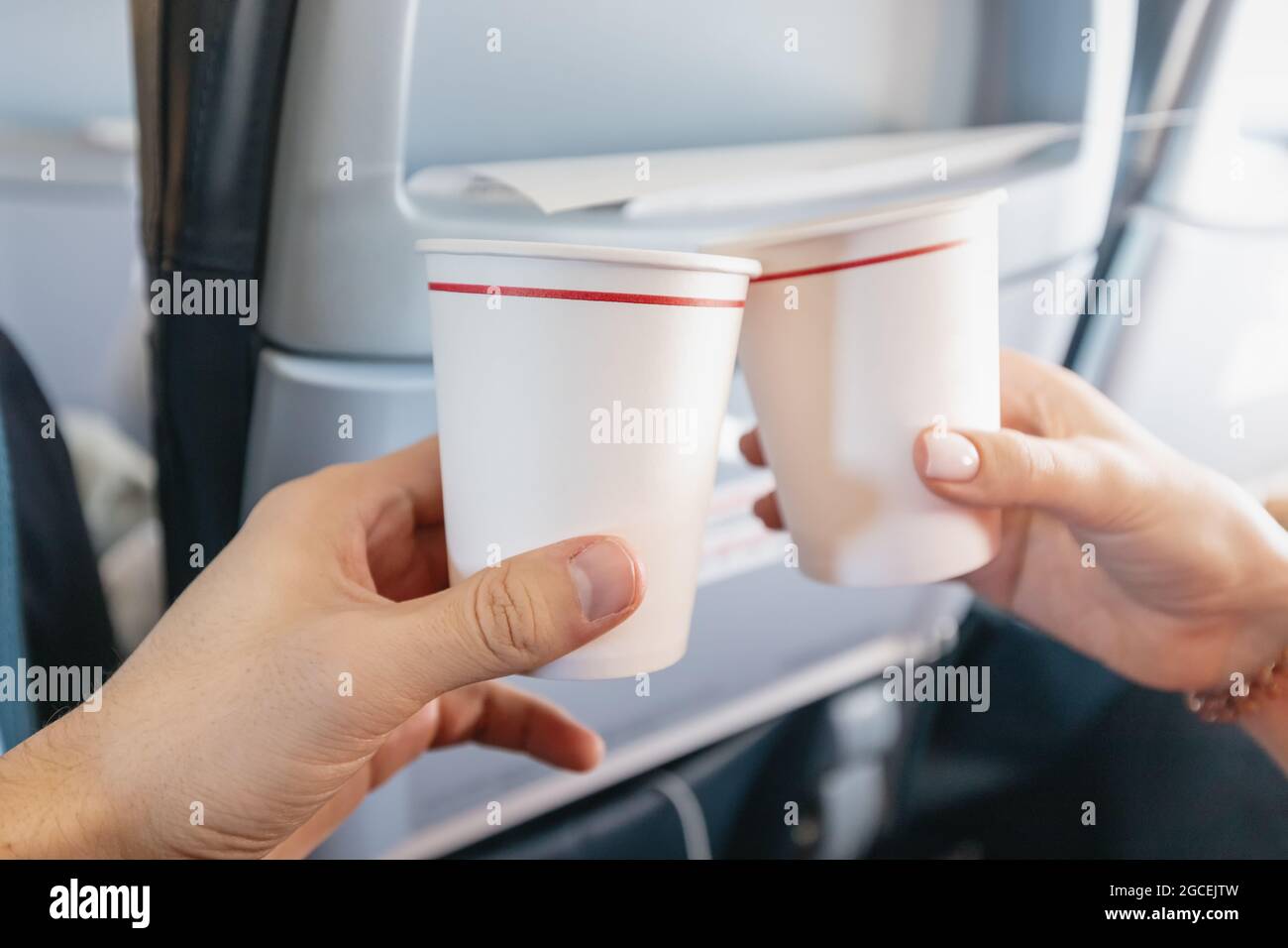 Ein glücklicher Mann und eine Frau klirken während eines Ferienfluges im Inneren eines Flugzeugs Pappbecher. Catering und Weinverkostung Stockfoto