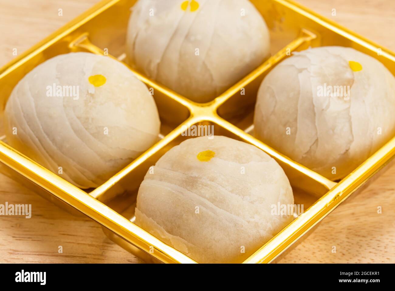 Chinesisches Gebäck oder Mondkuchen gefüllt mit süßer Mungbohnenpaste und gesalzenem Eigelb in goldener Schachtel auf Holztisch. Stockfoto