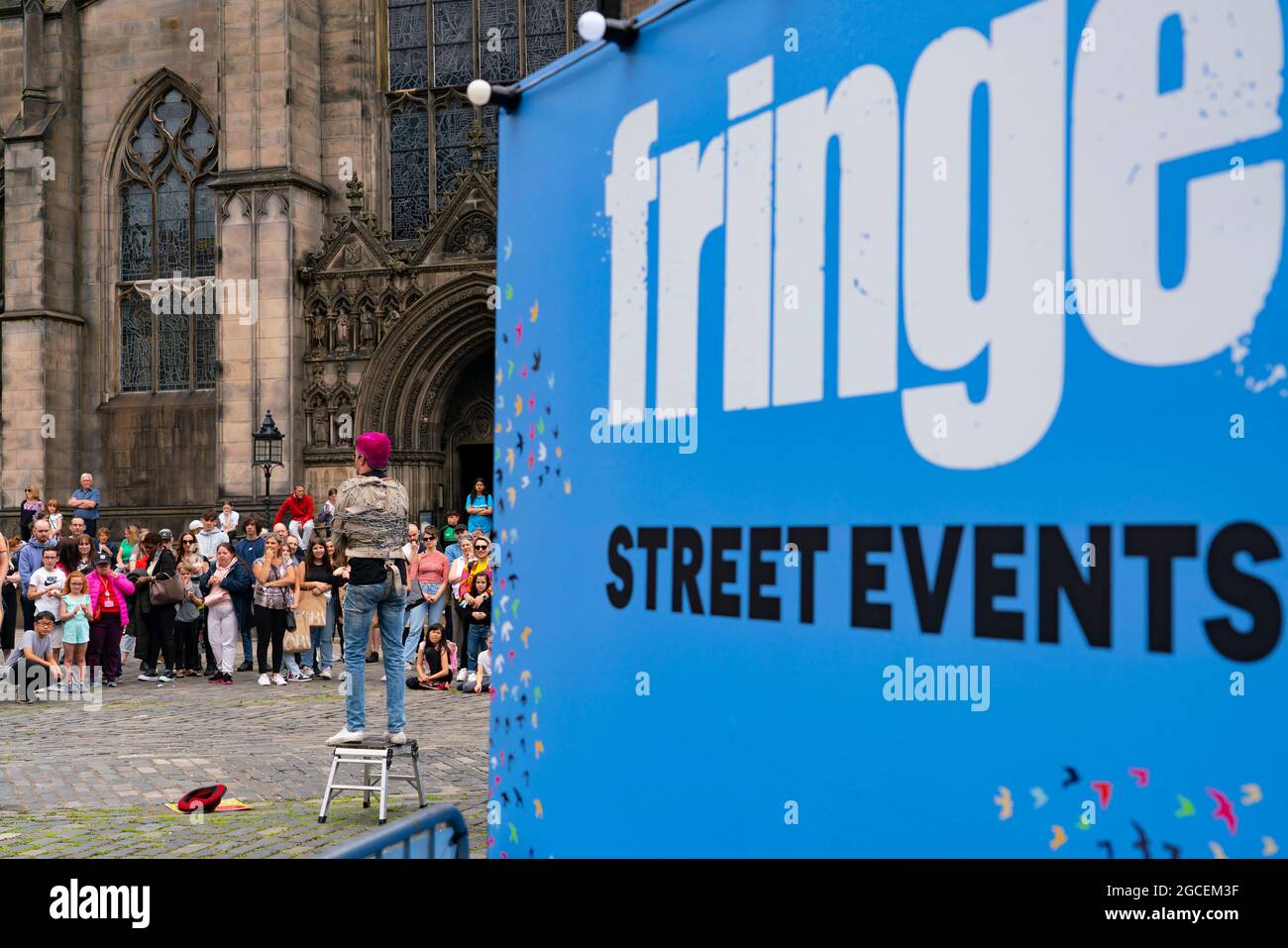 Edinburgh, Schottland, Großbritannien. August 2021. An einem sonnigen Sonntagnachmittag war die Royal Mile voll mit Besuchern, die auf der Suche nach der begrenzten Straßenunterhaltung waren, die während des viel zurückgehenkten Edinburgh Fringe Festivals in diesem Jahr geboten wurde. Zwei Bühnen sind für Darsteller vorgesehen und diese erwiesen sich den ganzen Tag über als beliebt. Bild: Die Menge beobachtet den Darsteller auf dem Parliament Square vor der St. Giles Cathedral. . Iain Masterton/Alamy Live Nachrichten. Stockfoto