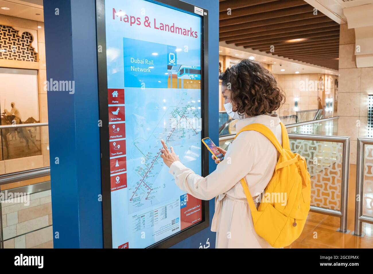 23. Februar 2021, Dubai, VAE: Frau mit einer medizinischen Schutzmaske wegen der Coronavirus-Pandemie sucht bei einem Selbstversorger nach einer Straßenbahn- oder U-Bahn-Route Stockfoto