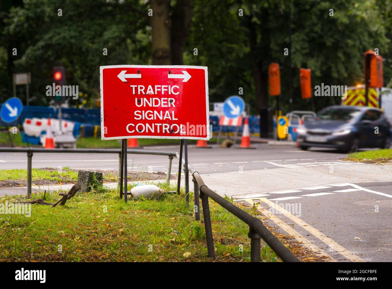 Ein Straßenschild an einer T-Kreuzung, das darauf hinweist, dass der Verkehr auf der Hauptfahrbahn aufgrund von Straßenbauarbeiten durch vorübergehende Ampeln kontrolliert wird Stockfoto