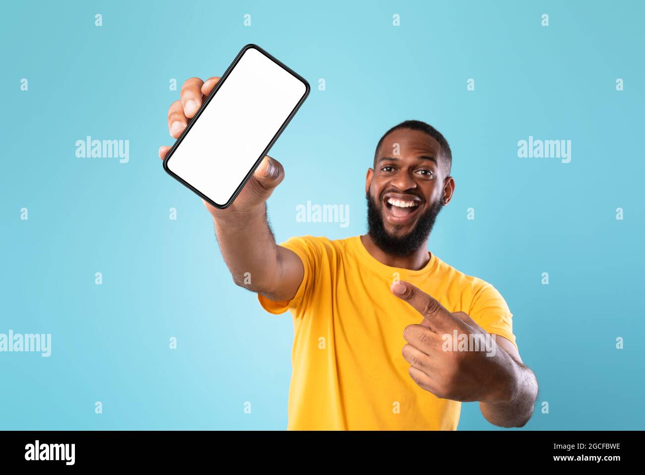 Neue tolle mobile App. Überglücklich schwarzer Kerl zeigt auf Smartphone mit leerem weißen Bildschirm auf blauem Hintergrund, mockup. Vorlage für die Anzeige von Mobiltelefonen, SPA Stockfoto