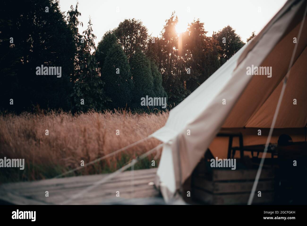 In einem Glockenzelt, das zum Glamping und Campen auf einem langen Grasfeld mit Sonnenuntergang hinter dem Zelt verwendet wird Stockfoto