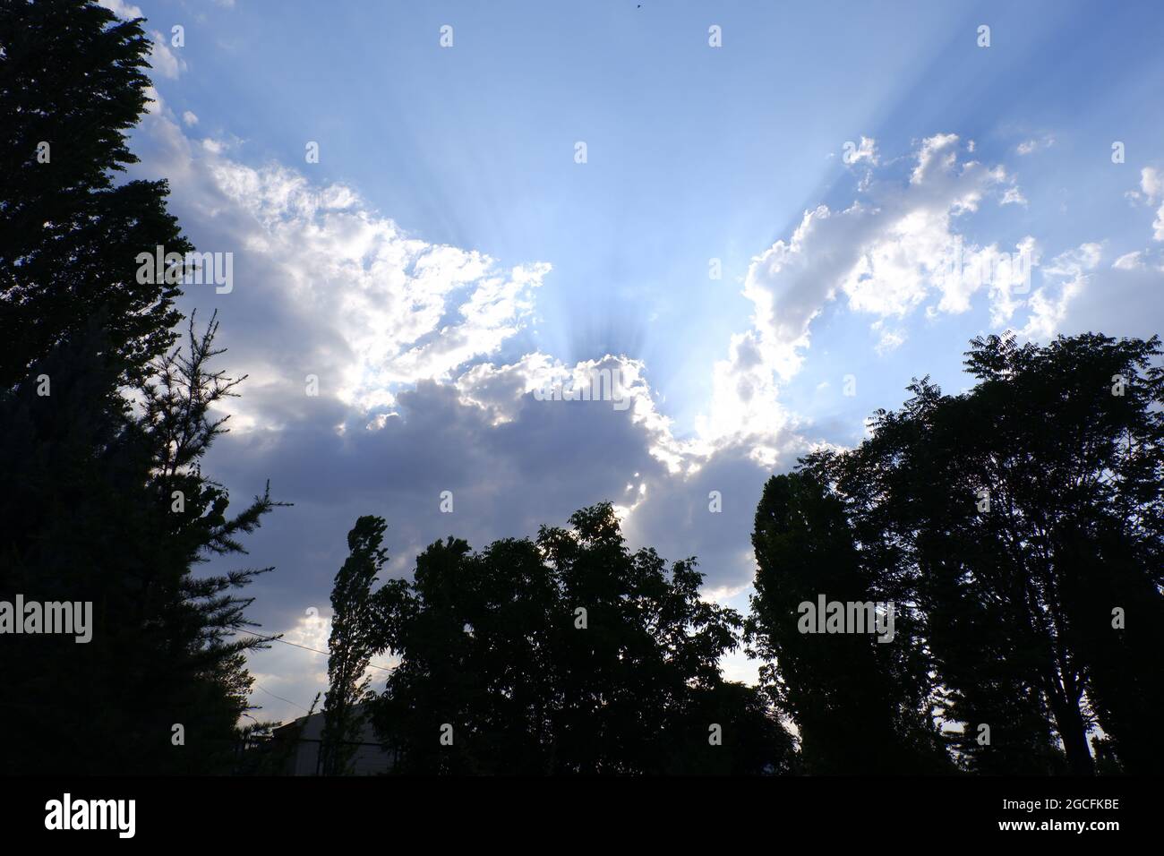 Sonnenstrahl hinter Wolken über Bäumen im Schatten Stockfoto