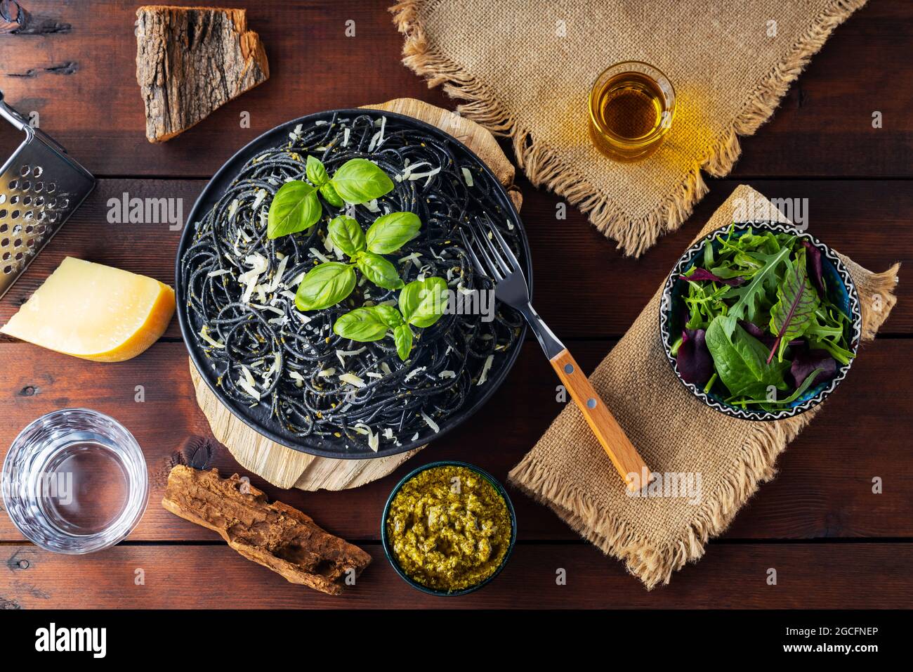 Pasta-Spaghetti mit Parmesankäse, Basilikum und Pesto-Sauce. Schwarze Pasta, Saucenpesto und frisch gemischter Salat aus Grüns auf Holzbrettern. Flach liegend. Oben vi Stockfoto