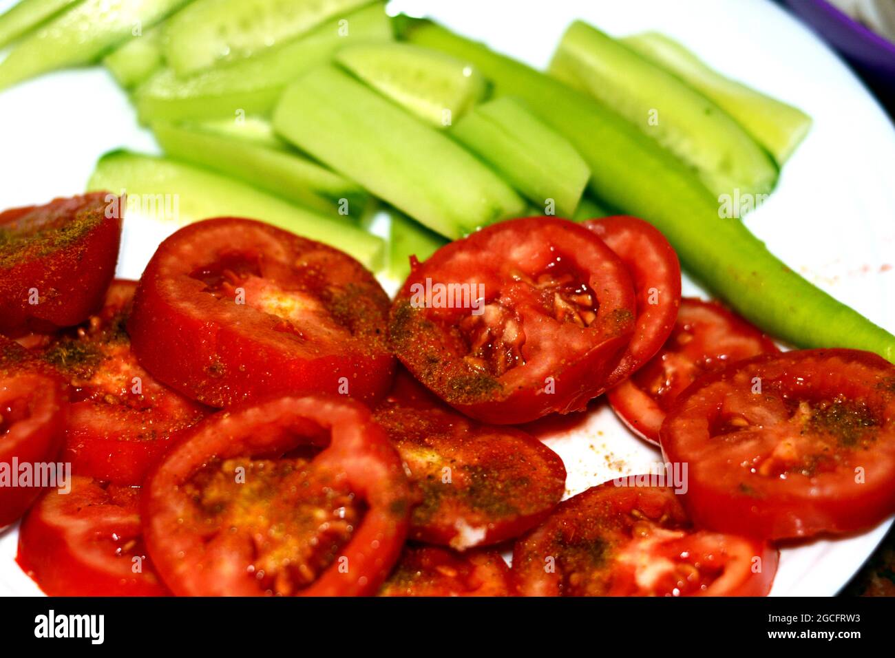 Scheiben gesalzener Tomaten mit Kreuzkümmel, Gurke und scharfem grünen Pfeffer auf einem weißen Teller, gesundes Lebensmittelkonzept, frisch geschnittene Tomaten und Gurken Stockfoto