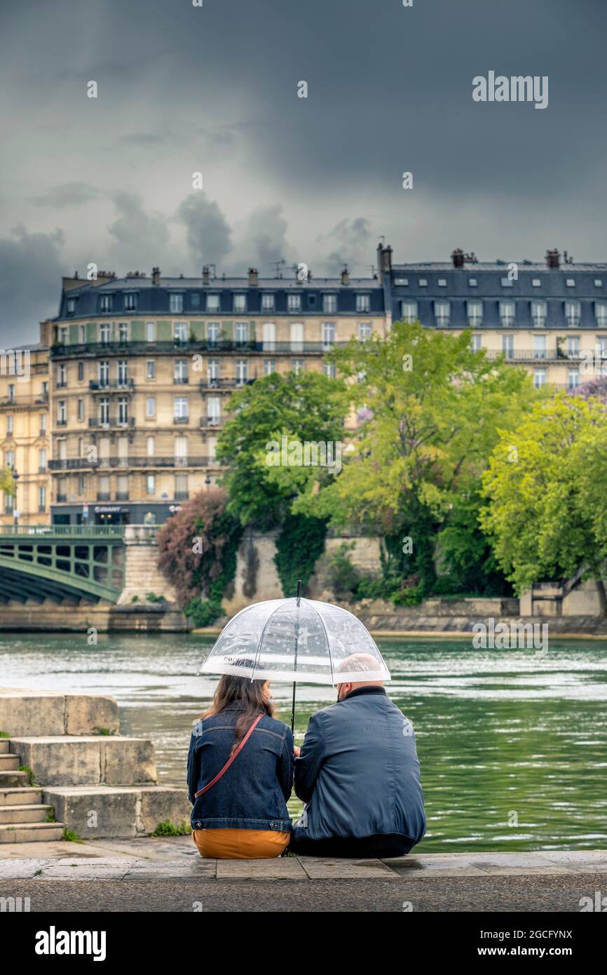 Paris, Frankreich - 1. August 2021: 2 Menschen nehmen mitten im Sommer in Paris an der seine Schutz unter ihrem Schirm Stockfoto