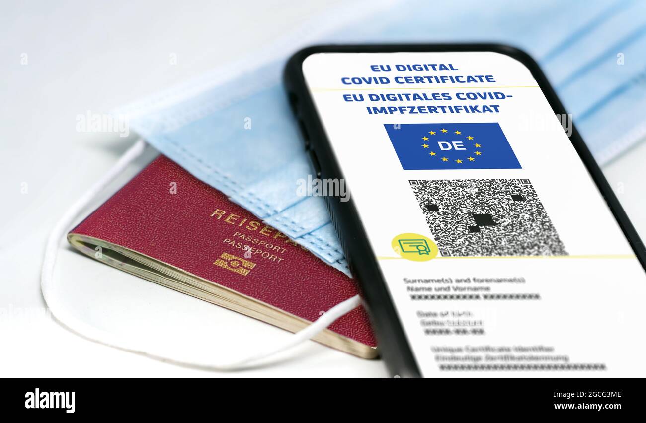Digitales EU-COVID-Zertifikat mit dem QR-Code auf dem Bildschirm eines Mobiltelefons über einer OP-Maske und einem deutschen Reisepass. Immunität gegen Covid-1 Stockfoto