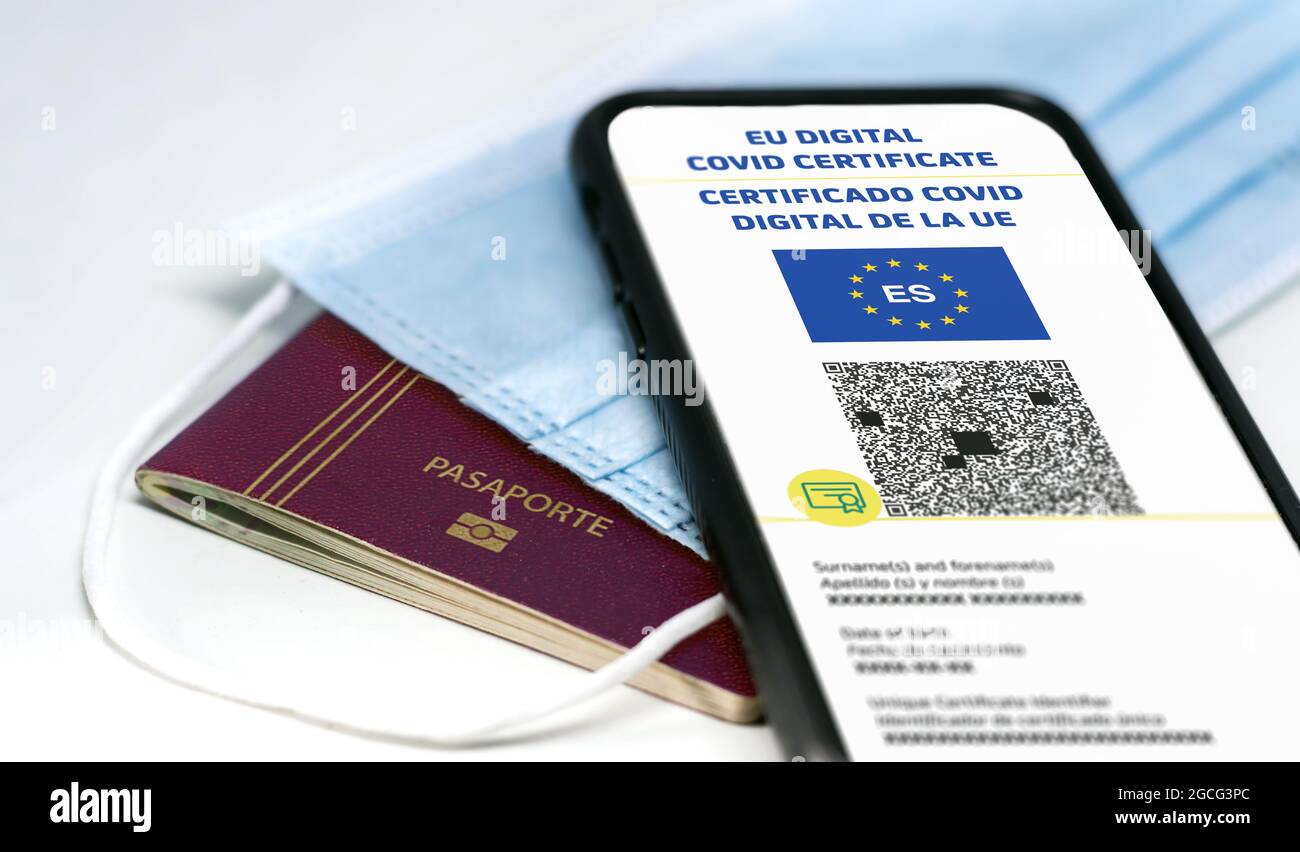 Spanish EU Digital COVID Certificate mit dem QR-Code auf dem Bildschirm eines Mobiltelefons über einer OP-Maske und einem spanischen Pass. Immunität gegen Covid Stockfoto