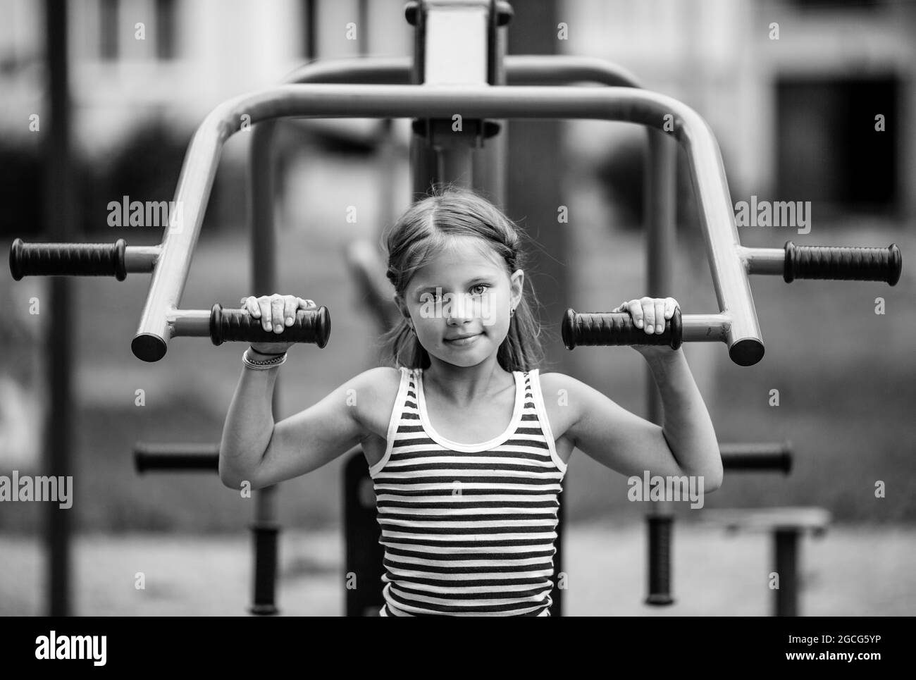 Kleines Mädchenportrait auf einer Trainermaschine auf dem Spielplatz im Freien. Schwarzweiß-Foto. Stockfoto