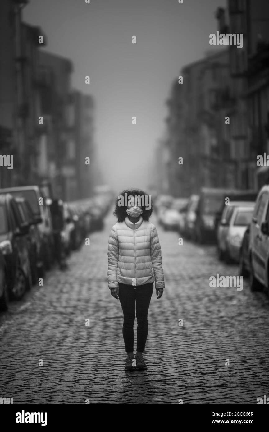 Asiatin in antiviraler Maske steht bei bewölktem Wetter auf der Straße. Schwarzweiß-Foto. Stockfoto