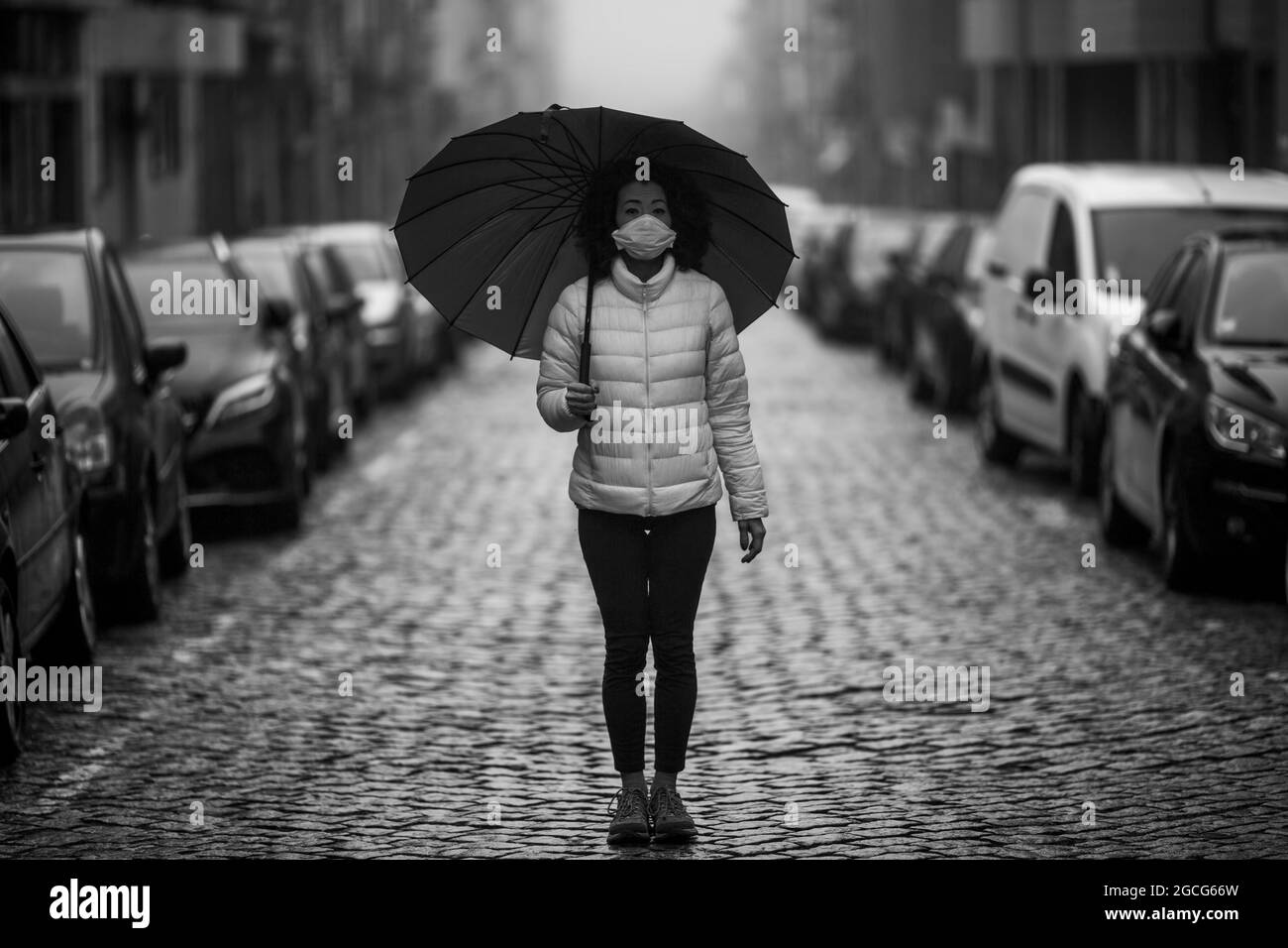 Multikulturelle Frau in antiviraler Maske steht bei bewölktem Wetter auf der Straße. Schwarzweiß-Foto. Stockfoto