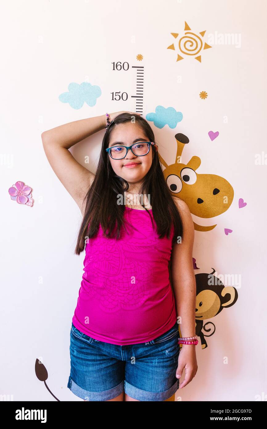 Hispanic teen girl with down syndrome measuring her height on the Wall, in disability concept in Latin America Stockfoto