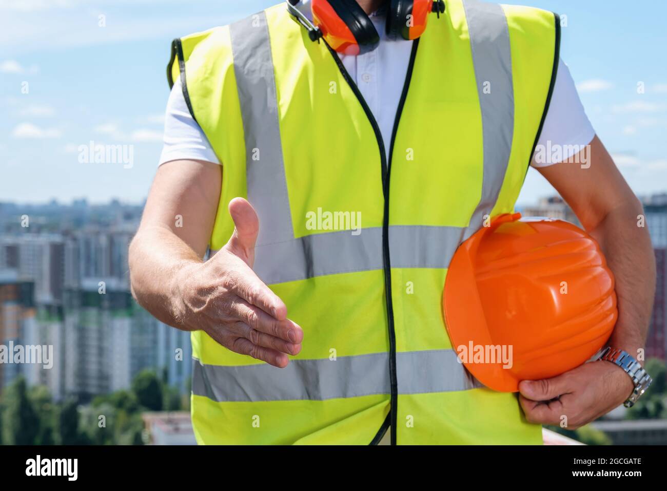 Der Baumeister hält eine Hand für einen Handschlag und die andere einen orangen Helm Stockfoto