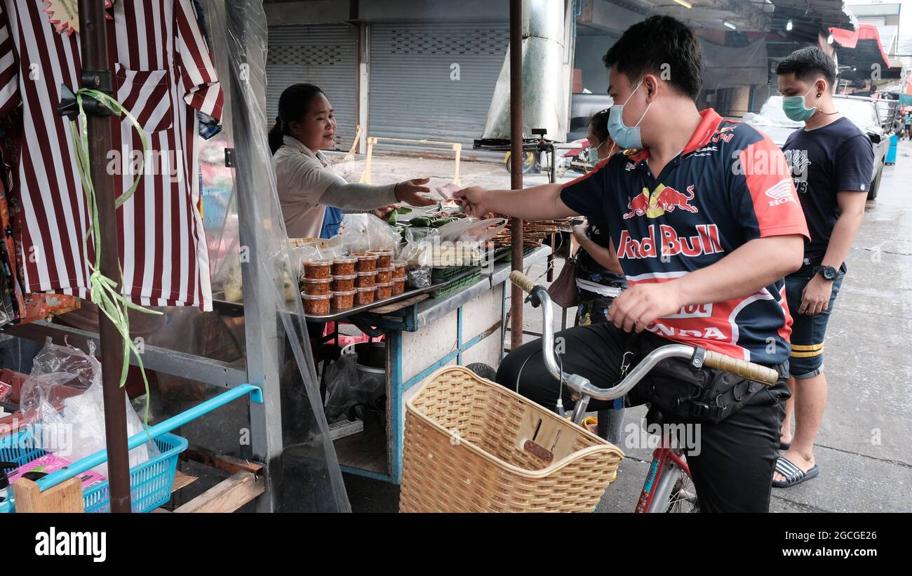 Mann auf dem Fahrrad, der einen Käufer des Racing Sport Shirts mit Bargeld in der Hand trägt, auf dem Klong Toey Market in Bangkok, Thailand Stockfoto