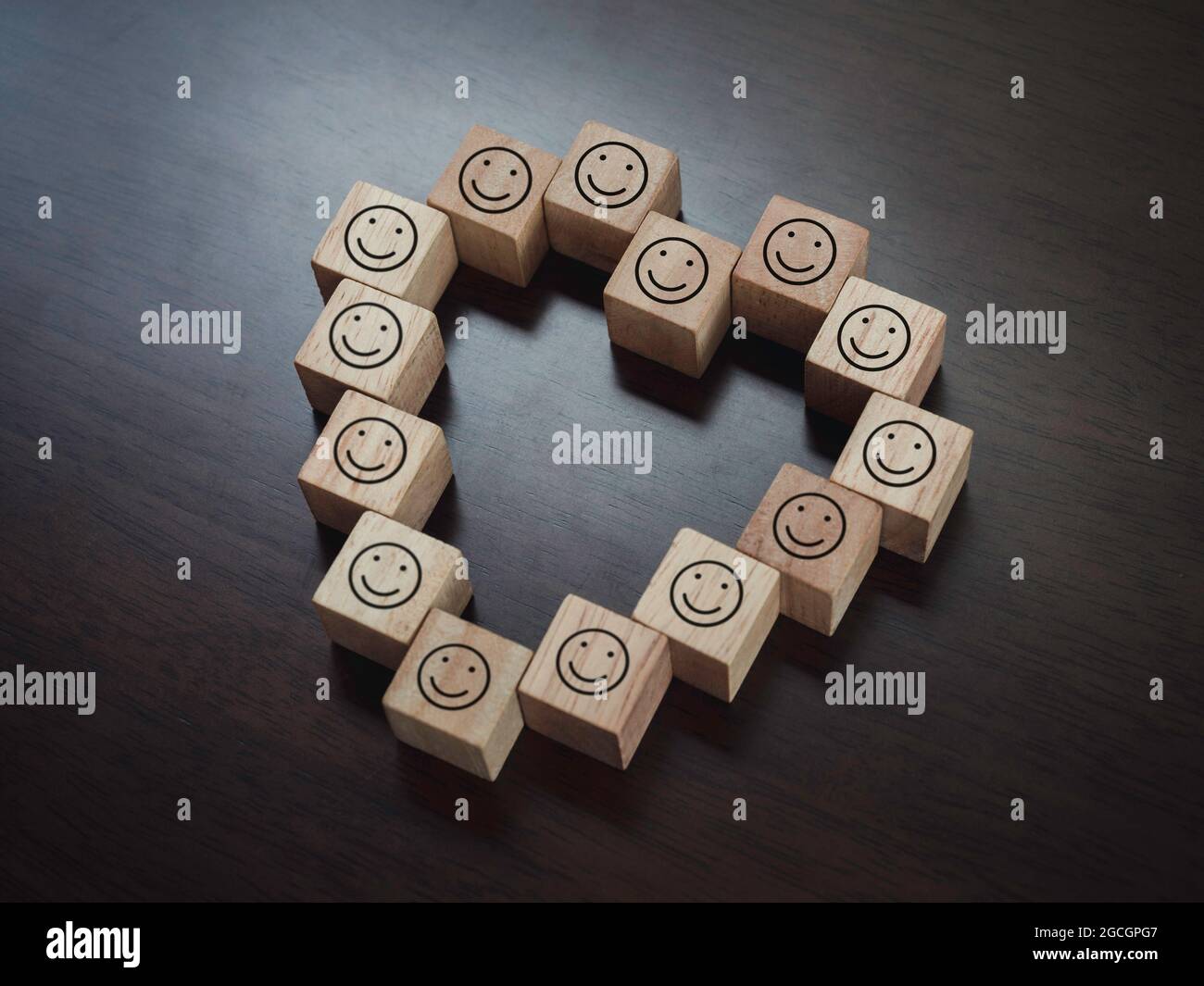 Holzklötze mit fröhlichem Lächeln im Gesicht, herzförmig auf dunklem Holzhintergrund, Draufsicht. Liebe und Koexistenz Konzept. Stockfoto
