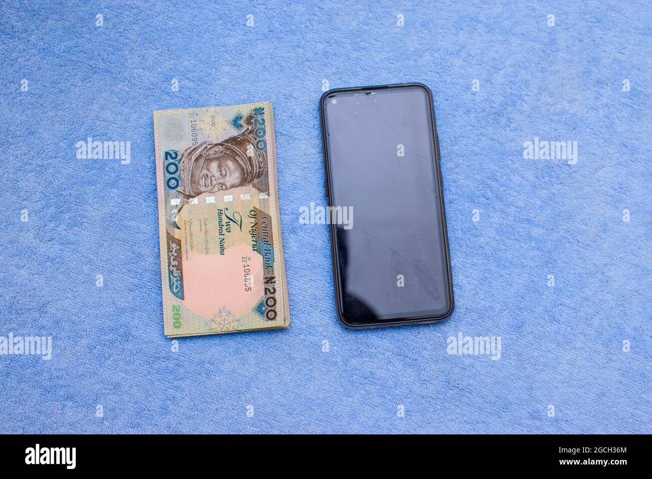 Mehrere Naira-Banknoten, Bargeld oder nigrische Währung mit einem Smartphone auf einer blauen Oberfläche platziert Stockfoto