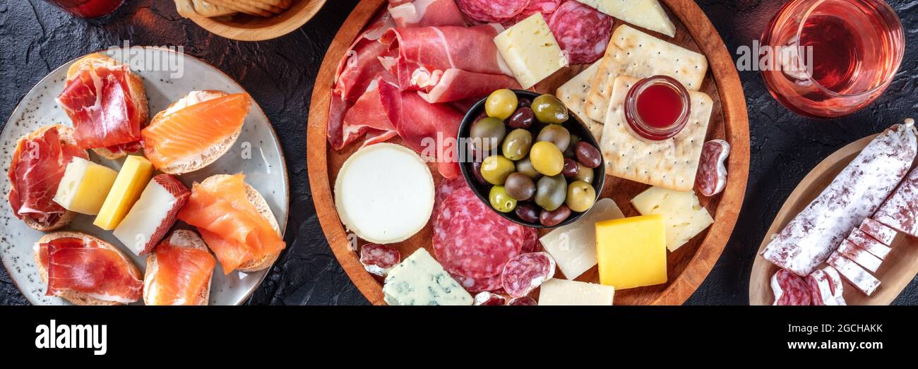 Panorama von Aufschnitt und Käseplatte mit Rosenwein und Lachs-Sandwiches, Top-Shot auf schwarzem Hintergrund. Ein Panorama-Banner für ein italienisches Antipasti-Restaurant Stockfoto