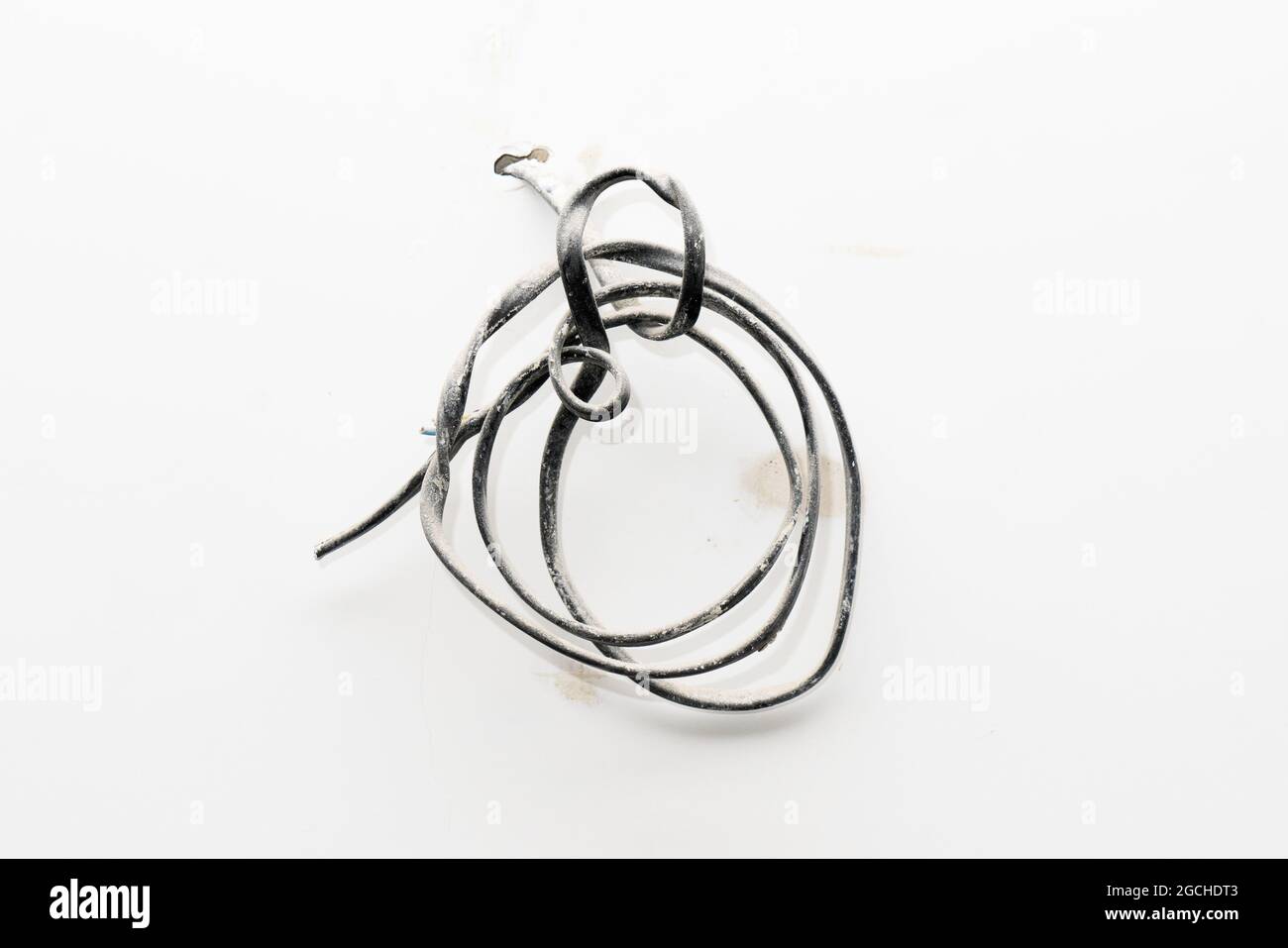 Dicker verdrillter schwarzer staubiger Draht, der aus der Wand ragt. Elektrokabel auf schmutzige weiß-grau-beige rohe raue Wand Stockfoto