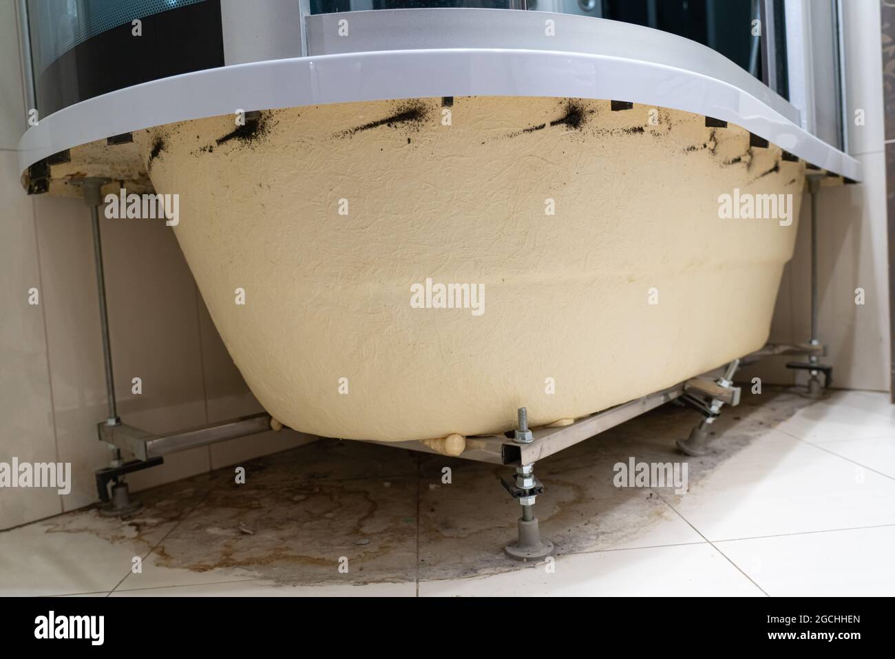 Schmutzige Pfütze, Schmutz, Haare, Staub, Schimmel, Bakterien, Pilze auf dem Boden unter dem Badezimmer. Innenseite der Acrylbadewanne ohne Zierpaneel. Rostig Stockfoto