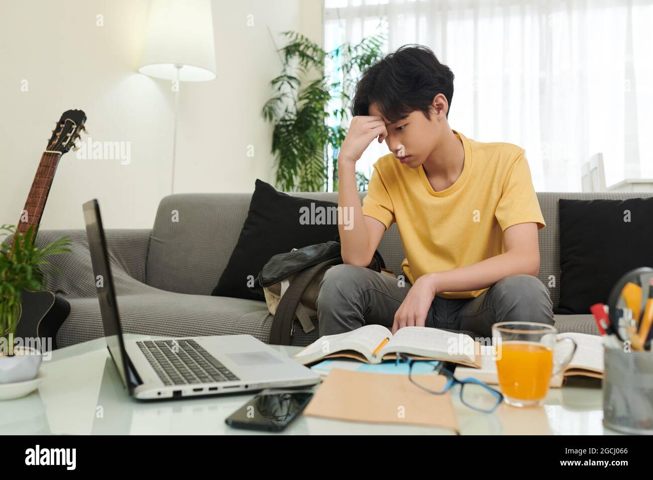 Gelangweilter Schuljunge, der es leid ist, mathematische Hausaufgaben für die Schule zu machen, sitzt auf dem Sofa und schaut auf den Laptop-Bildschirm Stockfoto
