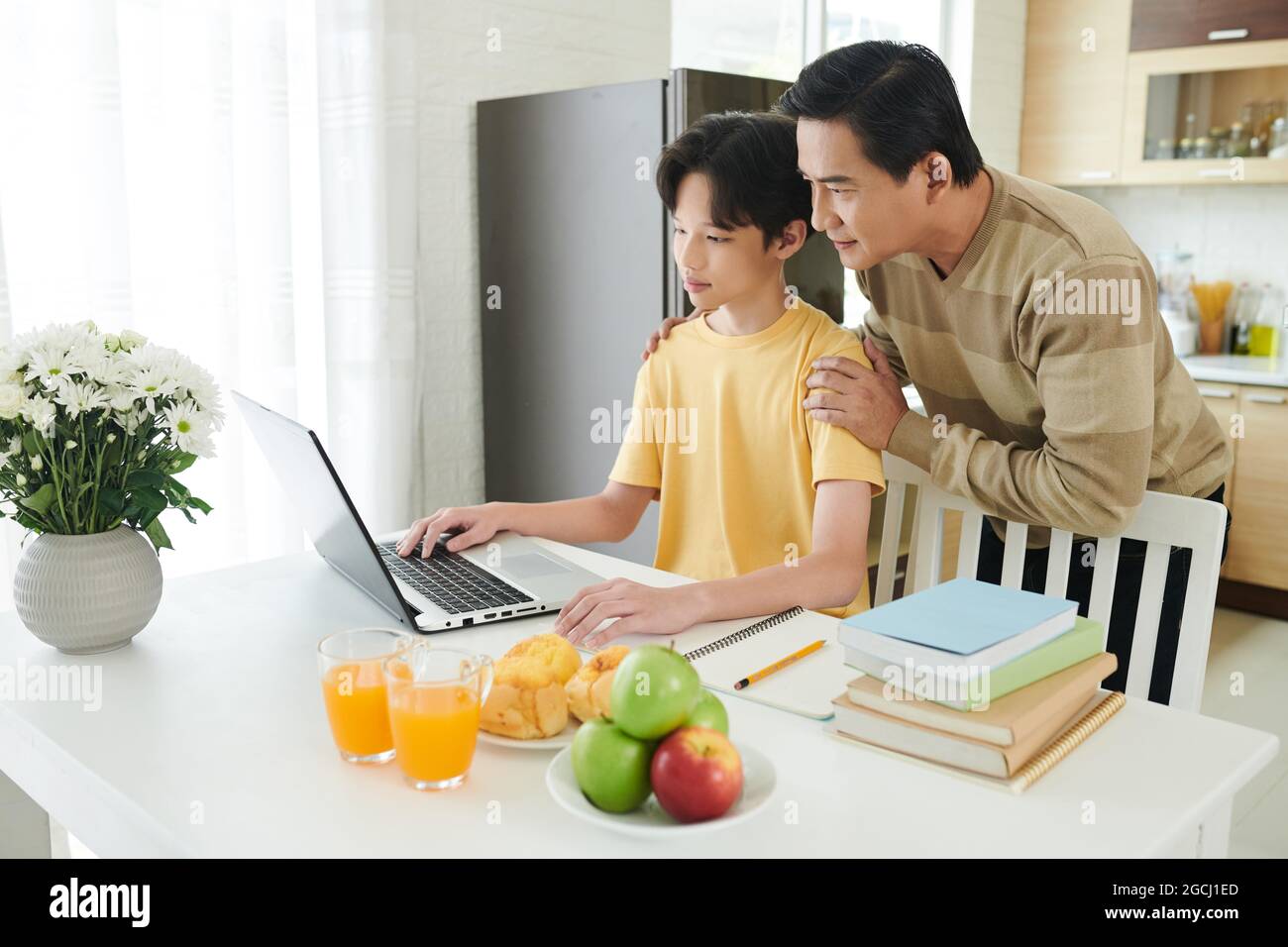 Stolzer Vater hilft seinem Sohn im Teenageralter bei der Hausaufgabe auf dem Laptop, wenn er aufgrund einer Pandemie online studiert Stockfoto
