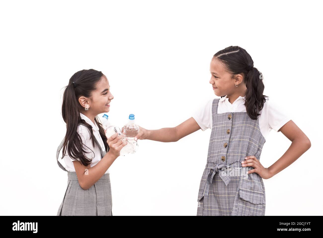 Zwei Schülerinnen in Uniform rösten mit Flaschen isoliert auf weißem Hintergrund Stockfoto