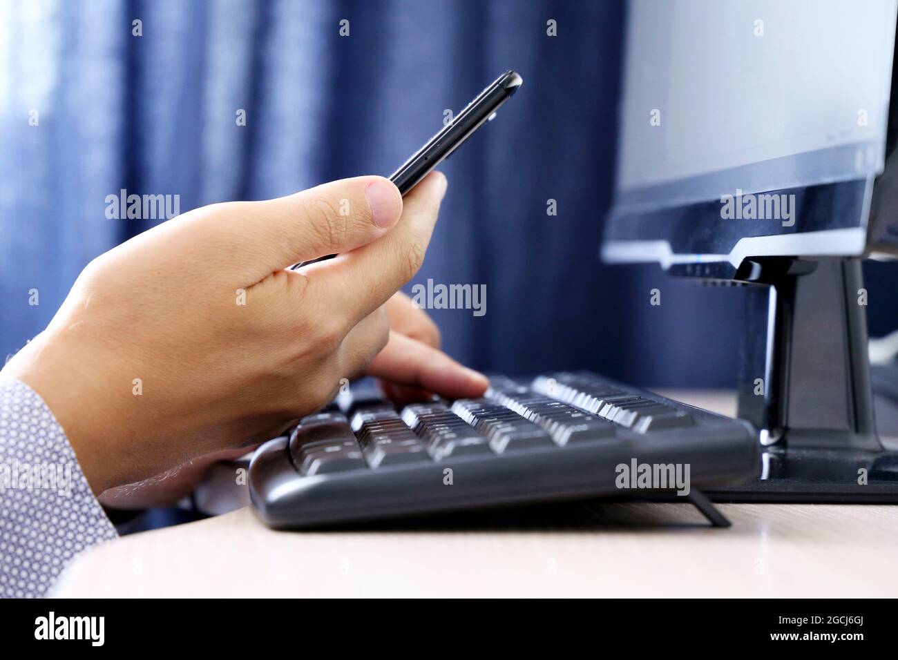 Mann mit Smartphone auf PC-Tastatur Hintergrund. Konzept der Online-Kommunikation, Büro- oder Heimarbeit und Bezahlung Stockfoto