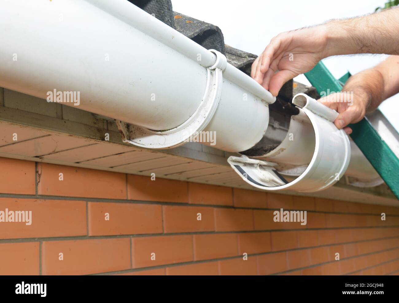 Installation und Reparatur der Dachrinne. Ein Mann auf einer Leiter ersetzt  ein Kunststoff-Regenrinnengelenk, eine Halterung, die die Dachrinnen  miteinander verbindet Stockfotografie - Alamy