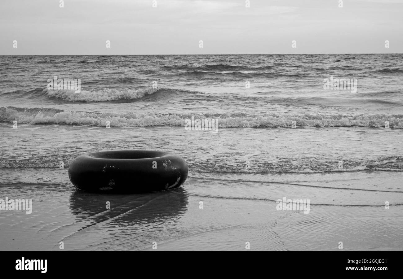 Einfarbiger schwarzer Schwimmring am Strand in Schwarz-Weiß-Tönen. Gummiring schwimmt im Meer mit Kopierraum. Stockfoto