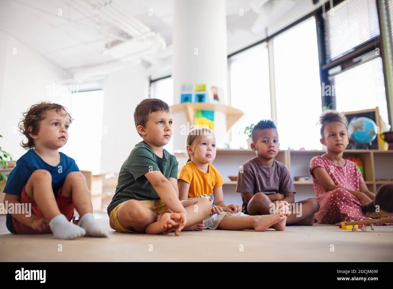 Gruppe von kleinen Kindergartenkindern, die im Klassenzimmer auf dem Boden sitzen. Stockfoto