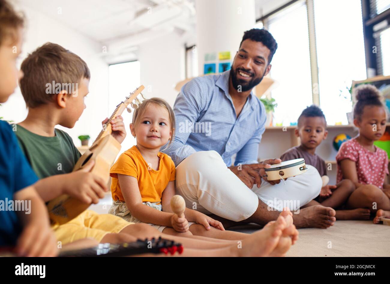 Gruppe von kleinen Kindern im Kindergarten mit einem Lehrer, der im Klassenzimmer auf dem Boden sitzt und spielt. Stockfoto