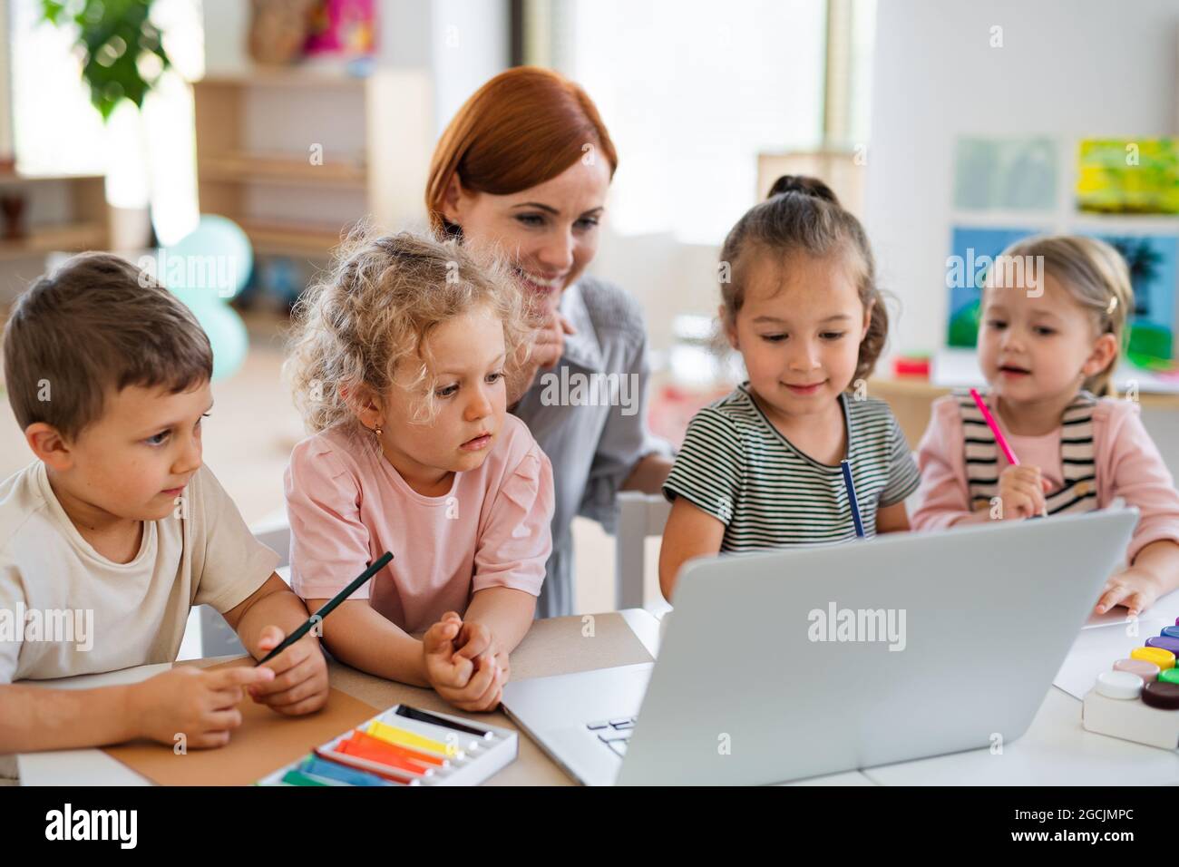 Gruppe von kleinen Kindern im Kindergarten mit Lehrer auf dem Boden drinnen im Klassenzimmer, mit Laptop. Stockfoto