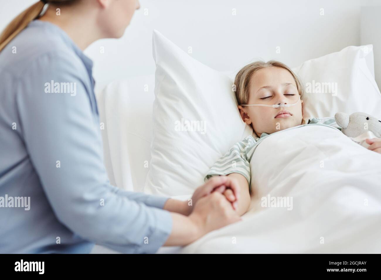 Porträt einer fürsorglichen Mutter, die die Hand des Kindes im Krankenhauszimmer mit Sauerstoffunterstützung hält Stockfoto