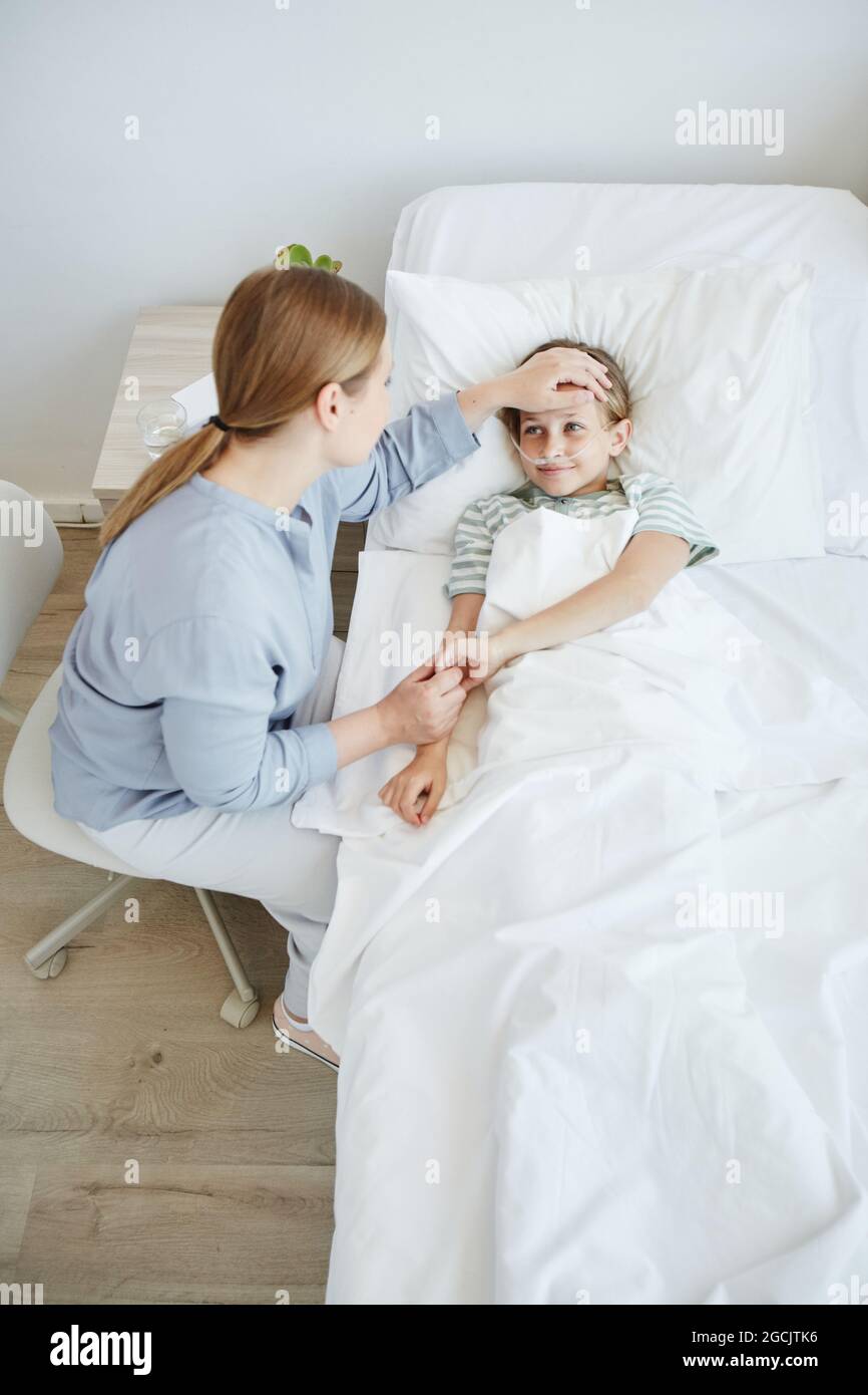 Hochwinkelporträt der fürsorglichen Mutter am Bett des kranken Kindes im Krankenhauszimmer, Fokus auf kleines Mädchen lächelnd Stockfoto