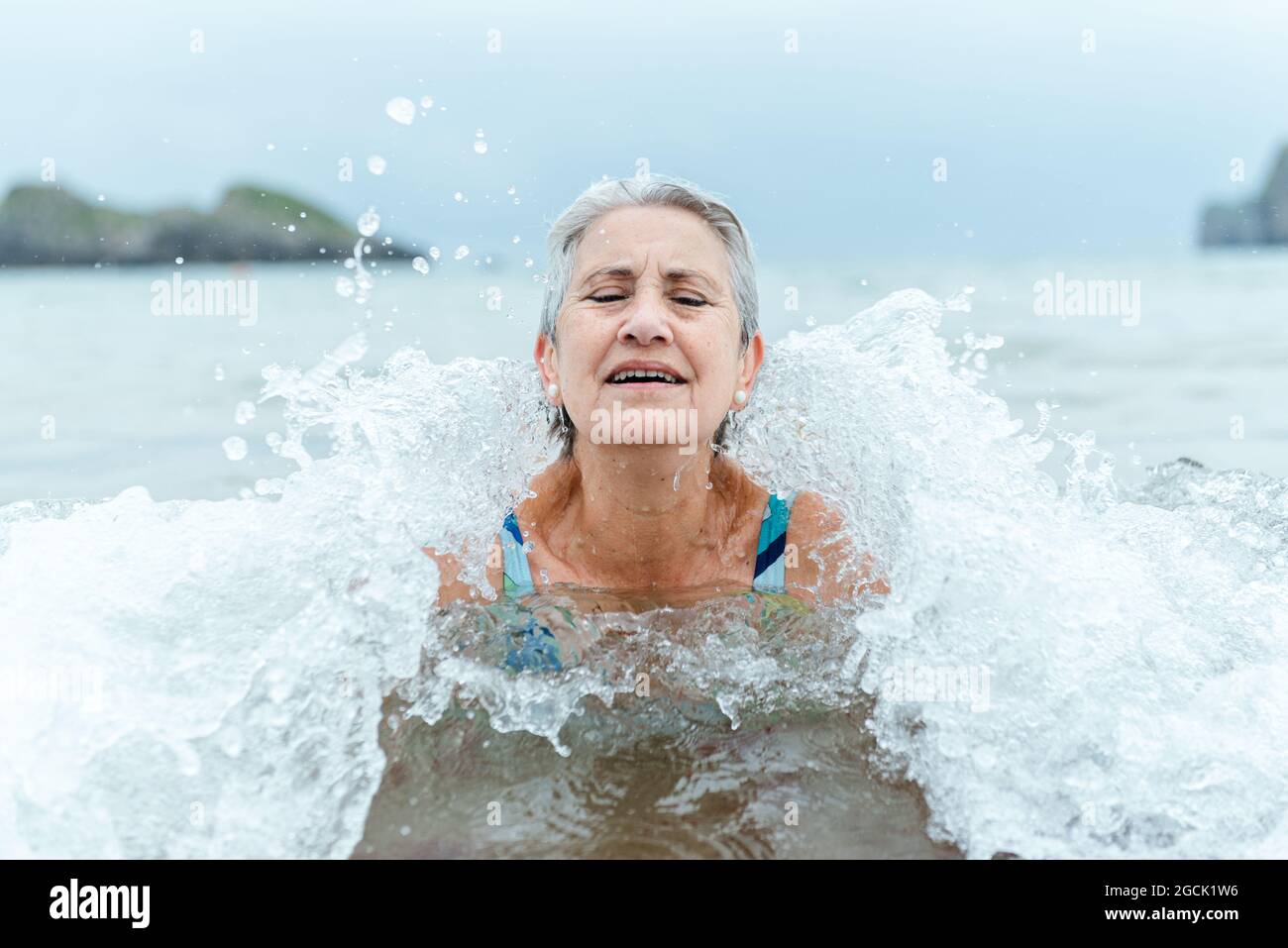 Aktive ältere grauhaarige Frau, die im Meerwasser schwimmt, während sie den Sommer genießt und an der Küste einen gesunden Lebensstil praktiziert Stockfoto