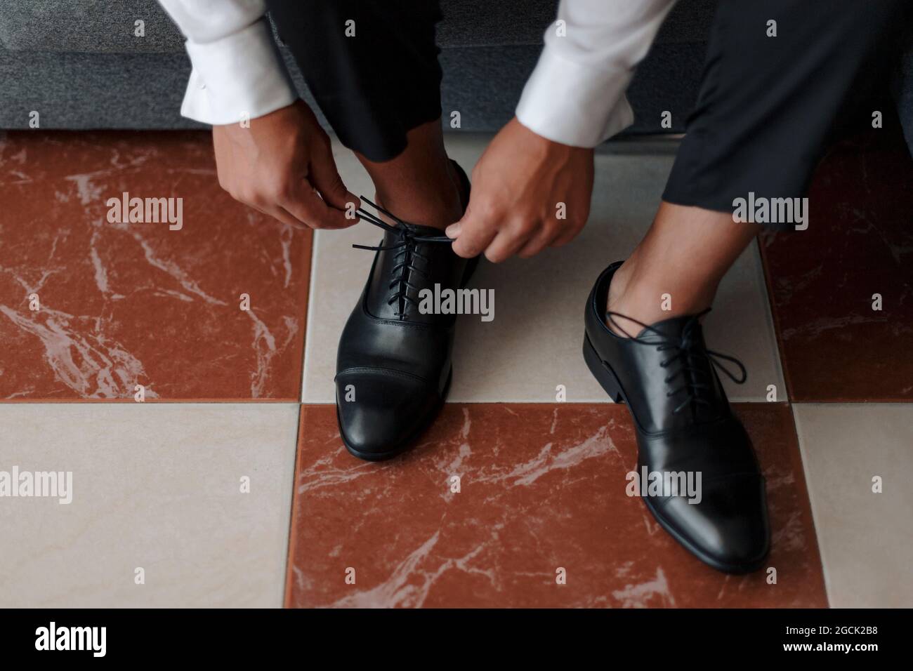 Von oben Crop anonyme Gentleman in weißem Hemd binden Schnürsenkel auf edlen schwarzen Lederschuhen Stockfoto