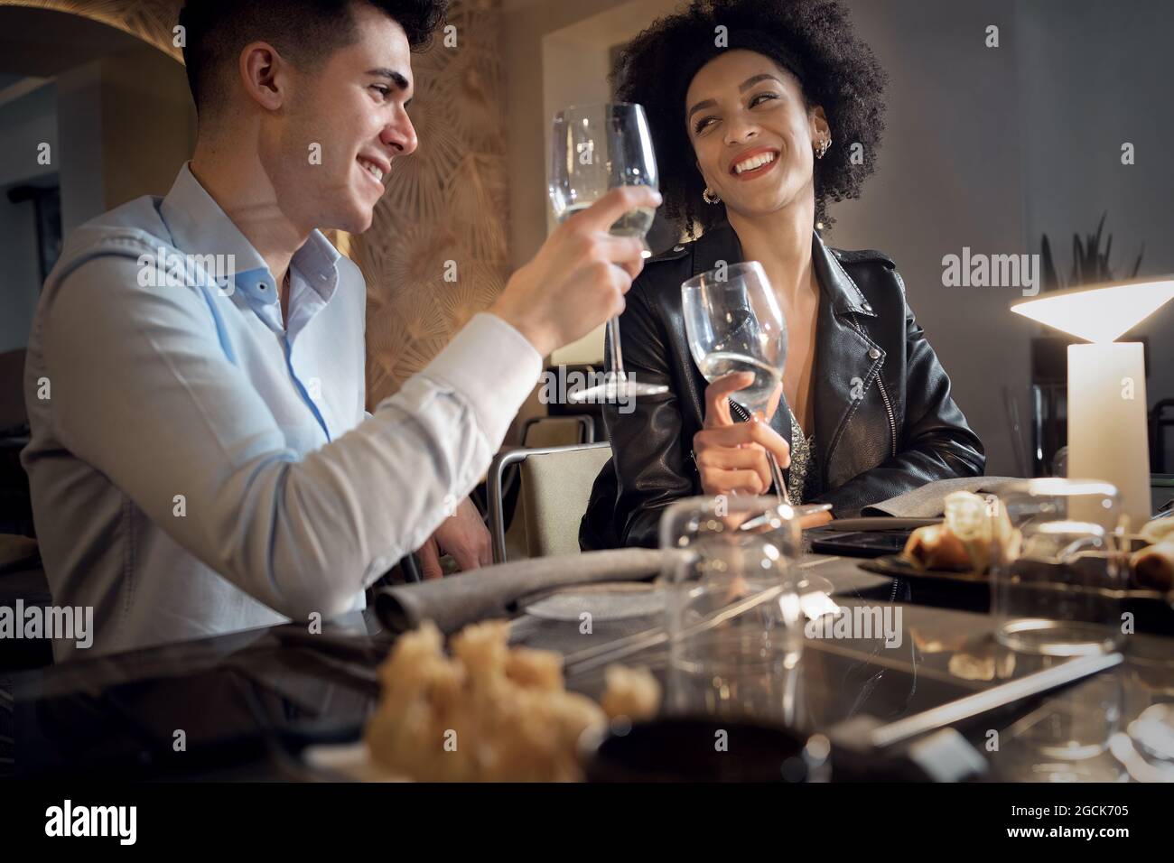Glückliches interrassisches Paar, das Spaß hat, im Fusion Food Restaurant zu reden, zu essen und zu trinken. Junge Leute aus klirrenden Weinläsern. Stockfoto