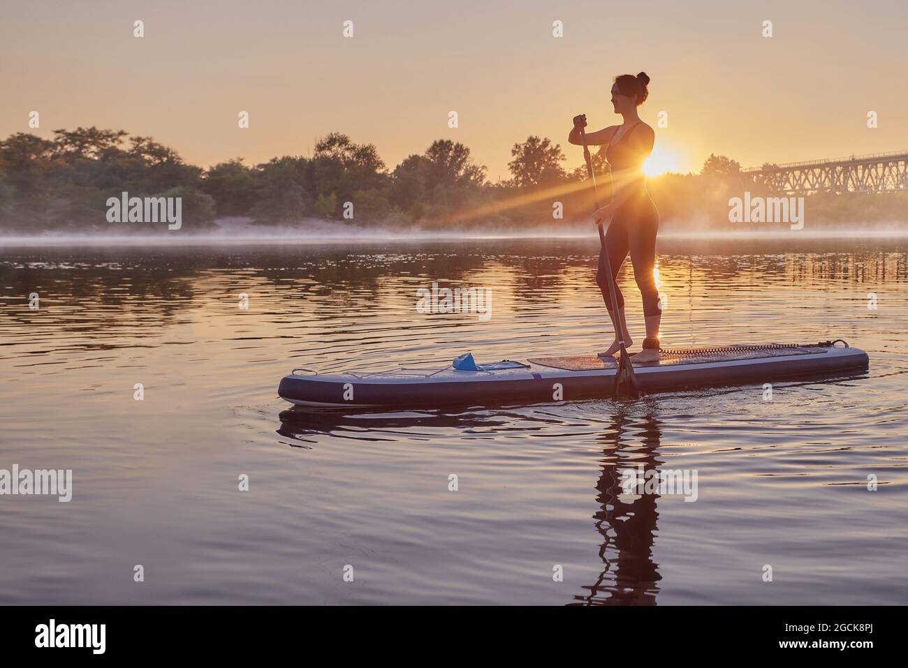 Frau paddelt auf einem SUP-Board auf dem Fluss, während Sonnenaufgang mit Nebel unten. Stand Up Paddleboarding, Sup Surfing Stockfoto
