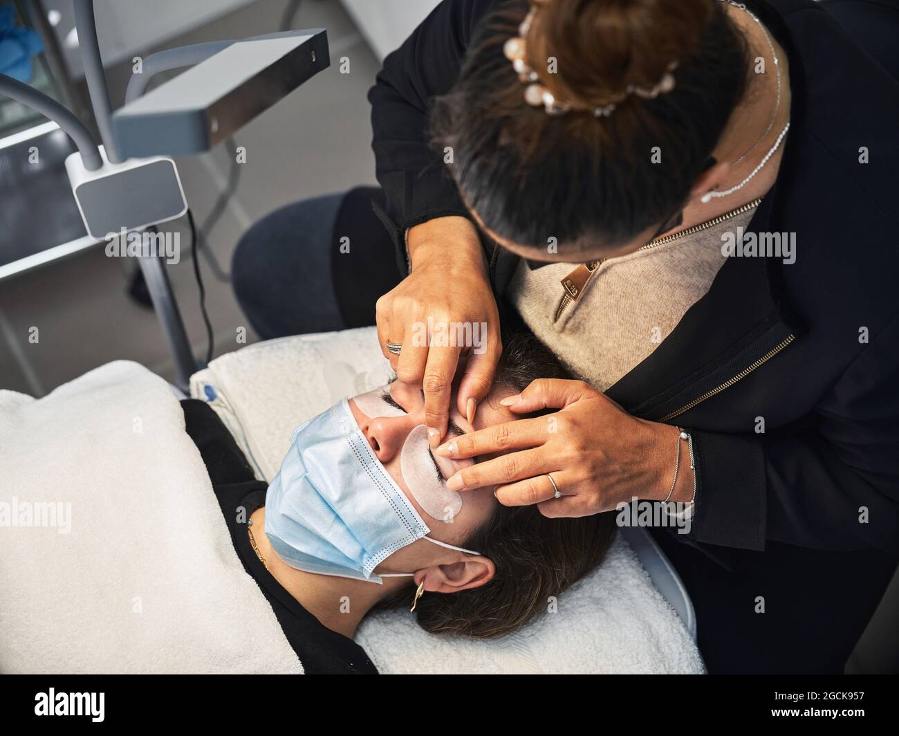 Fröhliche werdende Frau im Zierkleid sitzt auf Yoga-Ball Mit Kinderkleidung gegen Kommode im Zimmer Stockfoto