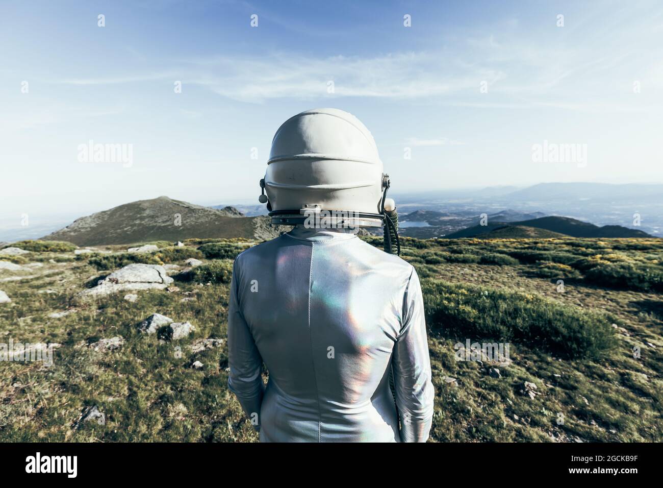 Rückansicht männlicher Astronaut in Raumanzügen und Helm, der auf Gras und Steinen im Hochland steht Stockfoto