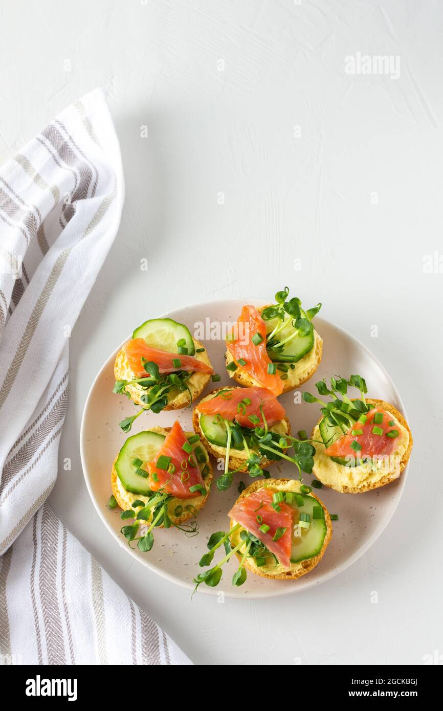 Leckere herzhafte Vorspeise, Lachsbraten auf einem weißen Teller, rundes gebratenes Brötchen mit rotem Fisch, Gurke, Sauce Hollandaise und Erbsensprossen Stockfoto