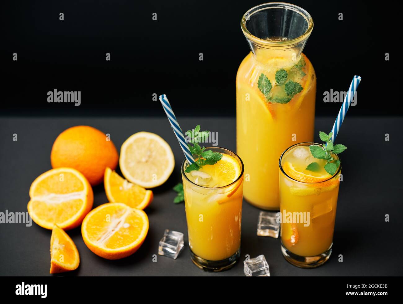 Köstlicher frischer Orangensaft mit Eis, Minze und frischen Früchten auf schwarzem Tischhintergrund. Party, Drink, Gesundheitskonzept Stockfoto